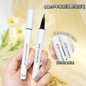 Hand holding white lambskin textured BOB eyeliner pen with black ink tip against soft floral background