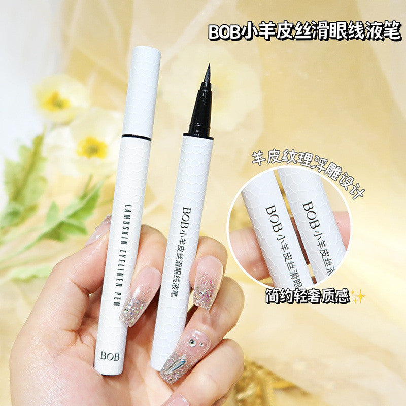 Hand holding white lambskin textured BOB eyeliner pen with black ink tip against soft floral background